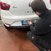 Foto zeigt Mitarbeiter der Dekra , der eine neue HU-Plakette klebt