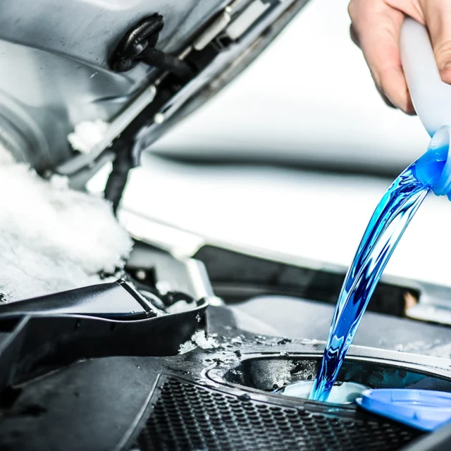Foto blauer Scheibenfrostschutz wird im Motorraum in Behälter eingefüllt