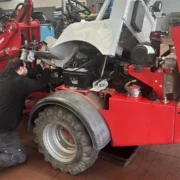 Foto zeigt Reparatur eines Weidemann-Traktors in Werkstatthalle mit davor knieendem Monteur